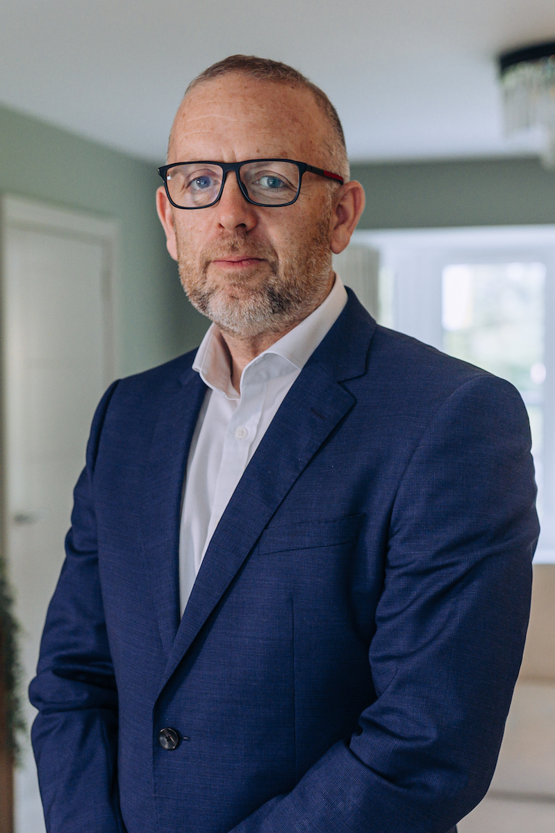 Peter in a blue suit standing in a living room, looking at the camera