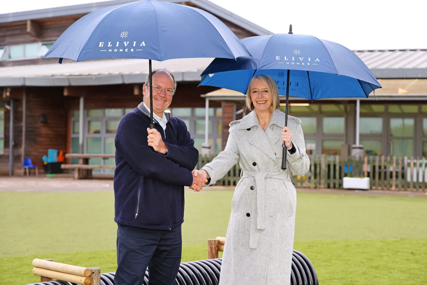 Elivia Homes colleague with school governor shaking hands on the new astroturf at Wivelsfield Primary School 